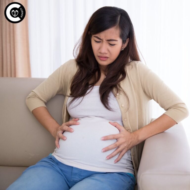 Pregnant woman holding abdomen in pain while sitting on bed, depicting miscarriage cramps